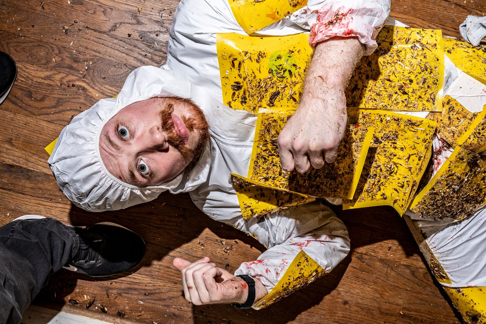 Photograph of a man on the ground wearing a hazmat suit with fly traps